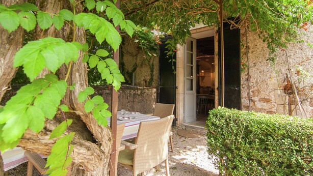 An outdoor dining area with a table and chairs, a stone wall, and a door leading to an interior space.