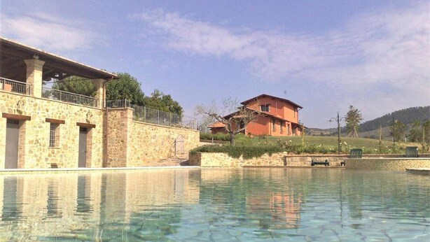 A stone building with a pool in front, a red house in the background, and a clear sky. - Apartment in Umbria with Infinity Pool Views (Bettona)