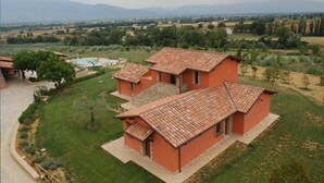 A two-story building with a tiled roof, surrounded by a well-maintained lawn and a swimming pool. - Apartment in Umbria with Infinity Pool Views (Bettona)
