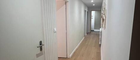 Um corredor com piso de madeira, paredes brancas e uma porta à esquerda.