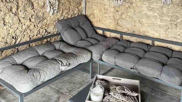 A room with a stone wall, a cushioned bench, and a small table with a container. - LE PETIT MONTY Gite Vue Étang 5 minutes from Puy Du Fou (Saint-Malô-du-Bois)