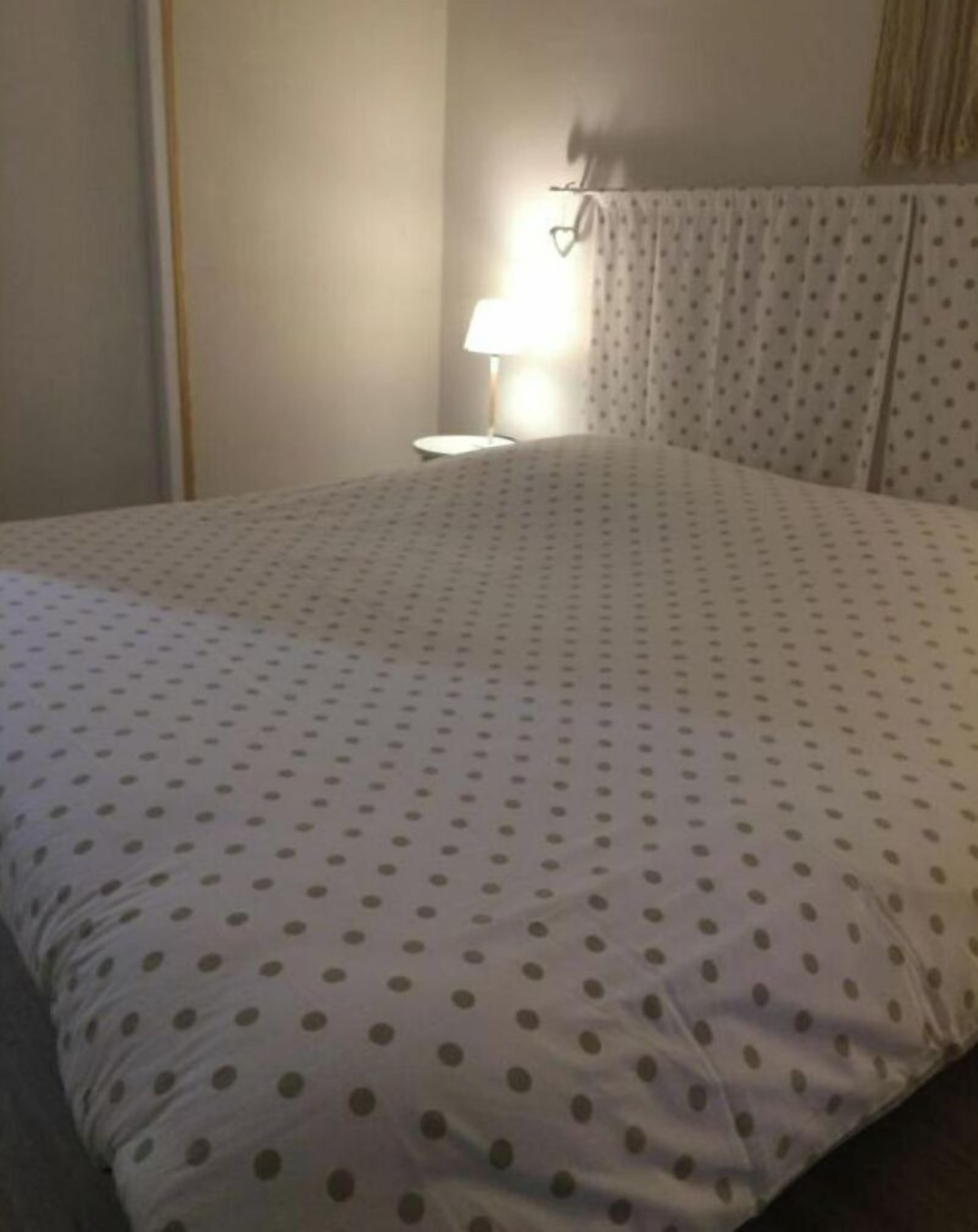 A hotel room with a bed covered in a polka dot duvet, a bedside lamp, and a curtain with a subtle pattern.
