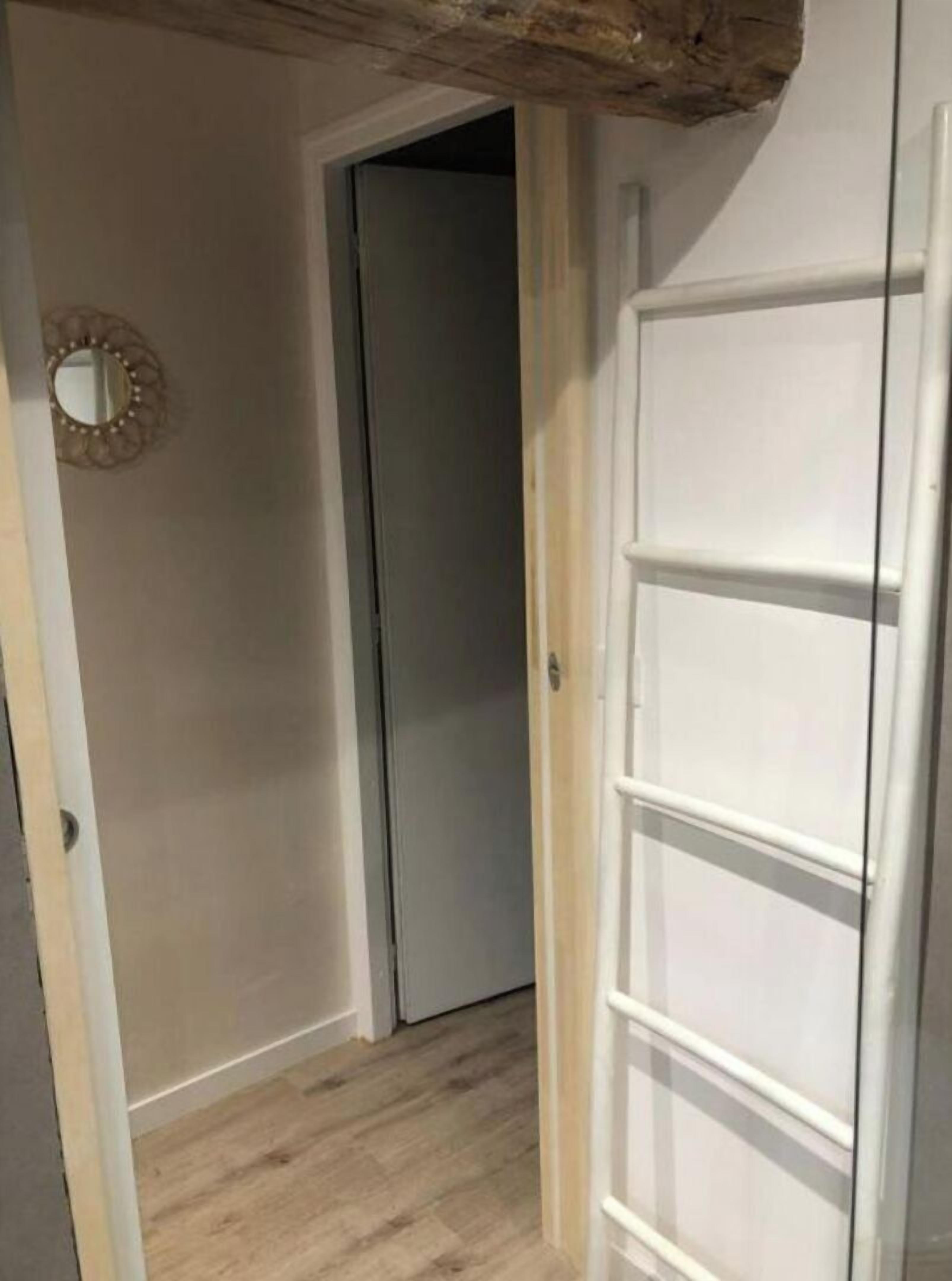 Ein schmaler Flur mit Holzboden, einer weißen Tür und einem Spiegel an der linken Wand.