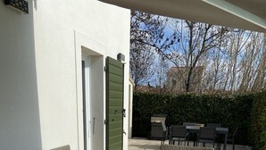 Eine Terrasse mit Korbmöbeln, einem Holztisch und einem Grill.