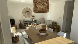 Ein Essbereich mit einem Holztisch, weißen Stühlen, einer gewebten Tischdekoration und einer Weidenleuchte.
