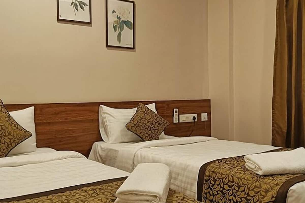 A hotel room with two single beds, a wooden headboard, a wall-mounted telephone, and two framed floral artworks.