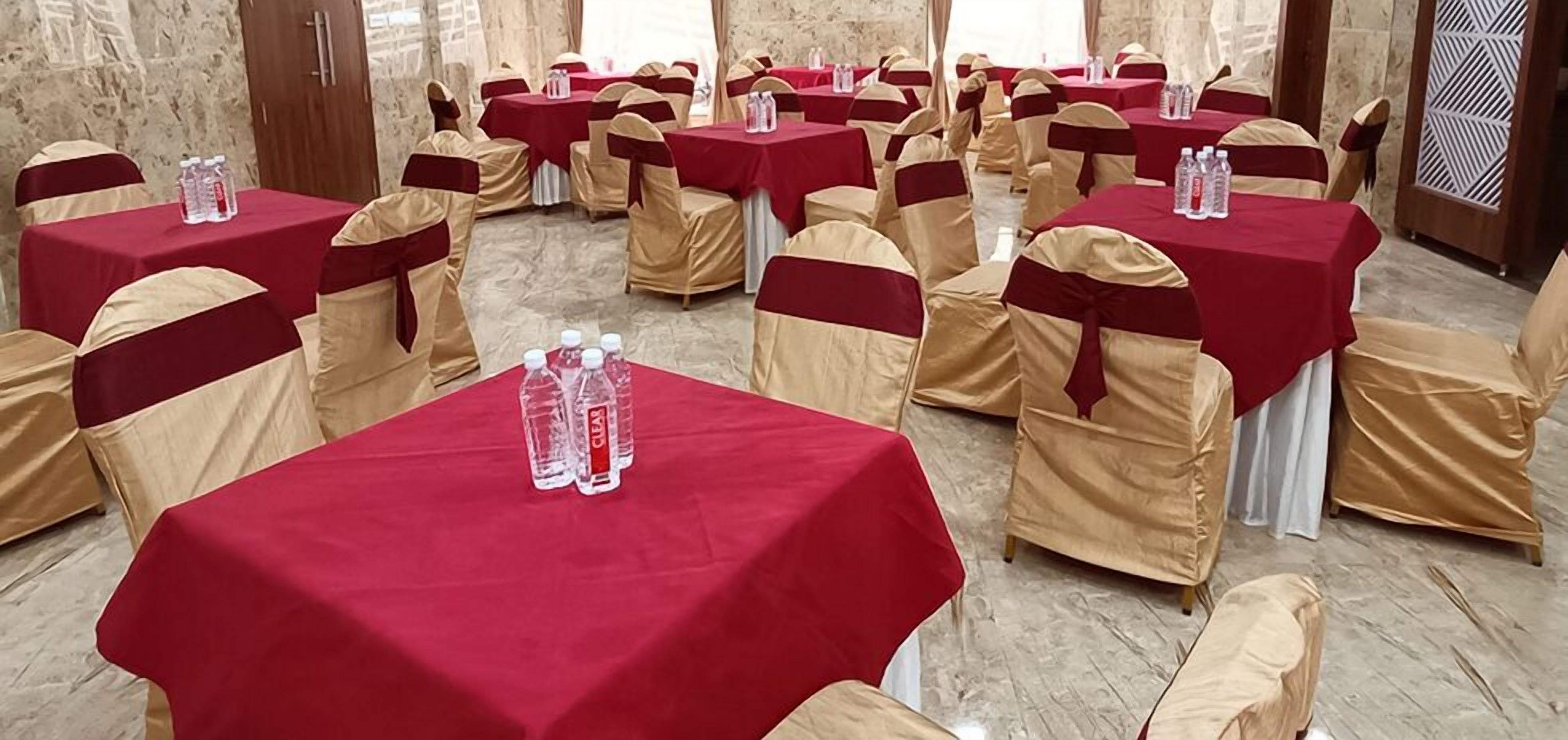 A banquet hall with tables covered in red tablecloths and chairs with beige and red sashes.