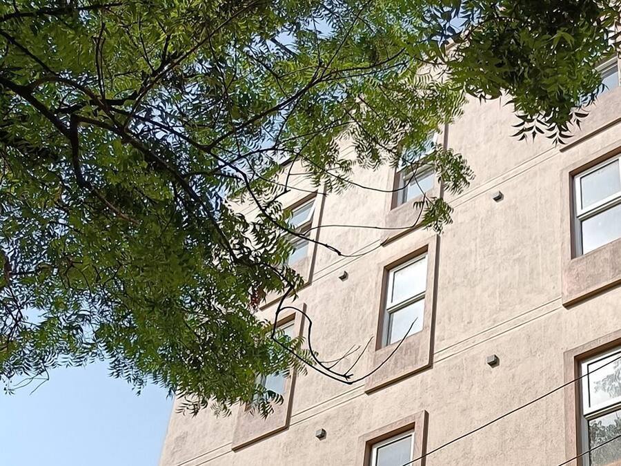 Un edificio de varios pisos con fachada color crema, varias ventanas y cables eléctricos a la vista.