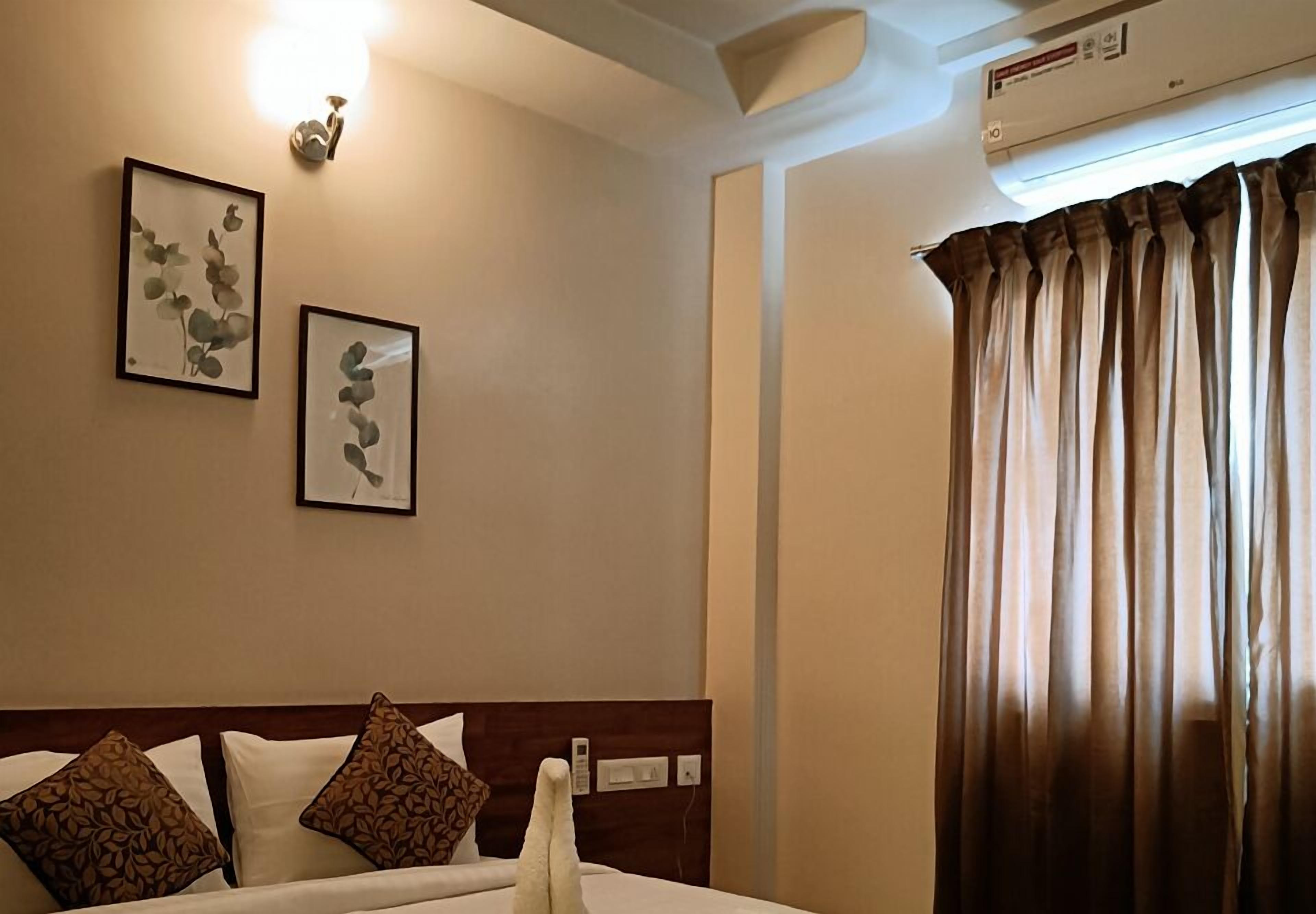 Een hotelkamer met een bed, twee kunstwerken aan de muur, een wandlamp, een airconditioner en een raam met gordijnen.