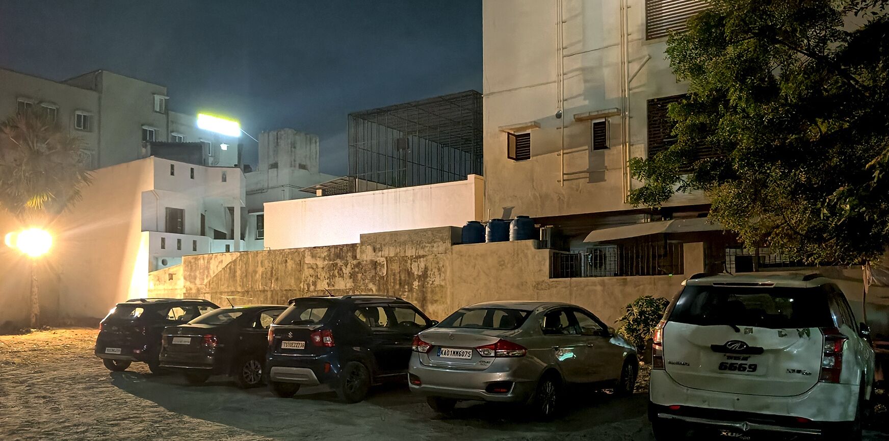 A parking area with several cars parked in front of a building with a concrete facade and multiple windows.