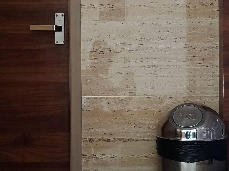 A room with a wooden door, a tiled wall, and a stainless steel trash bin with a black bag.