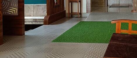 A modern interior with a patterned floor, a green rug, a wooden table, and a decorative wall panel.