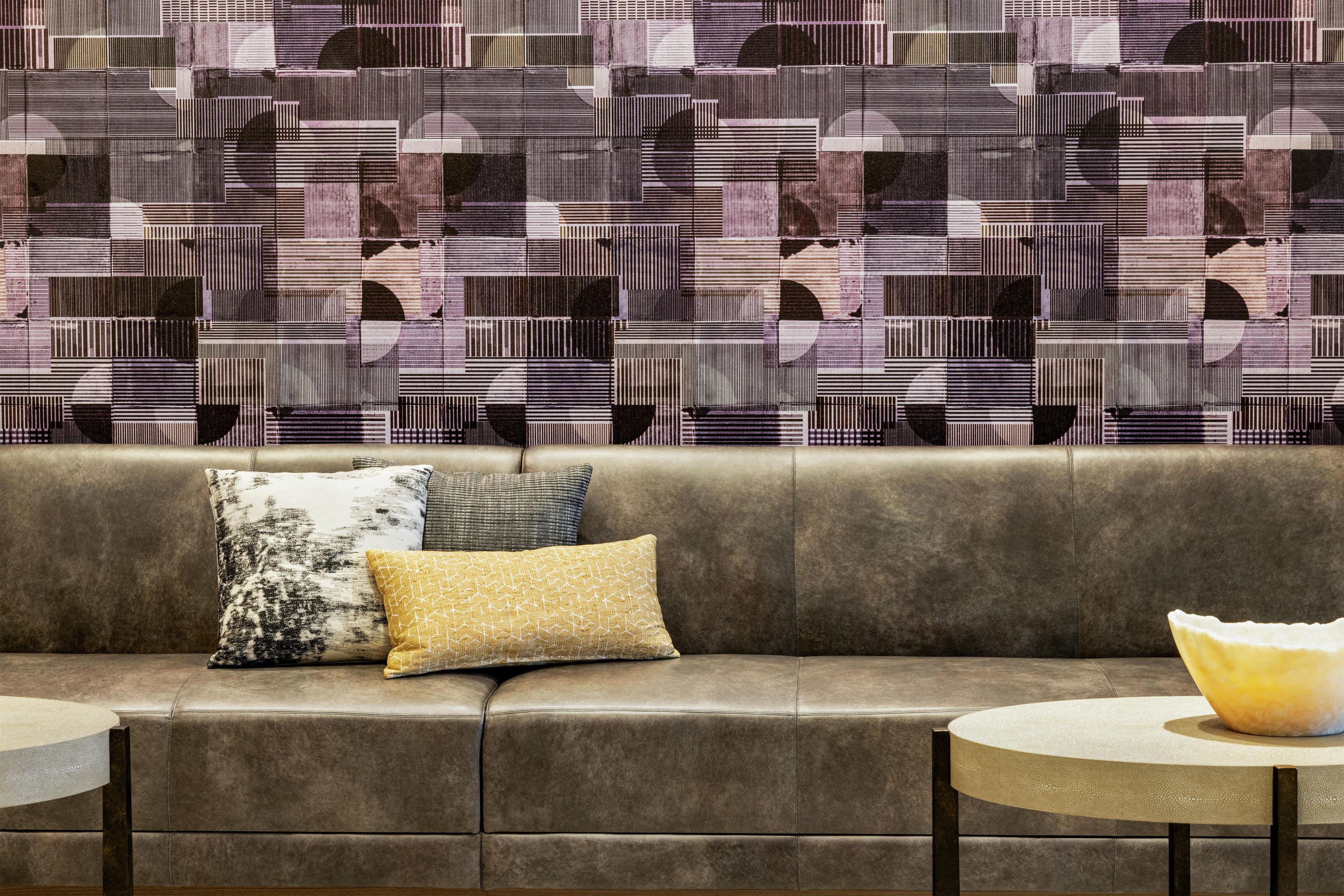 A modern interior with a patterned wall, a leather sofa with cushions, and a round table.