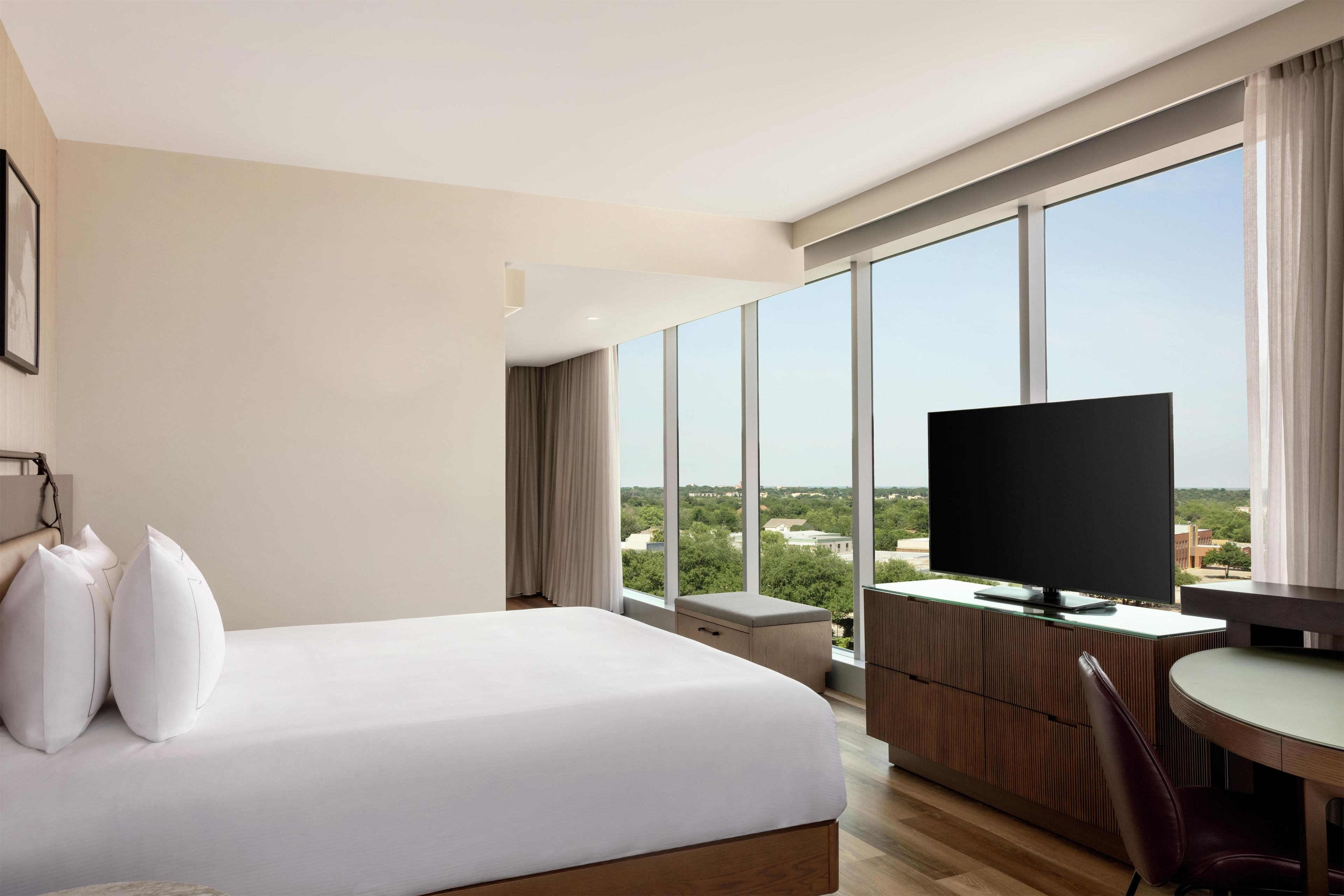 A hotel room with a large bed, a desk with a TV, and a view of the city.