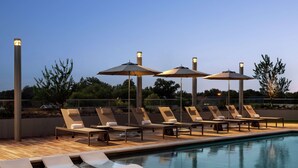 Un espace aménagé au bord de la piscine, avec des chaises longues et des parasols, une terrasse en bois et un ciel dégagé.