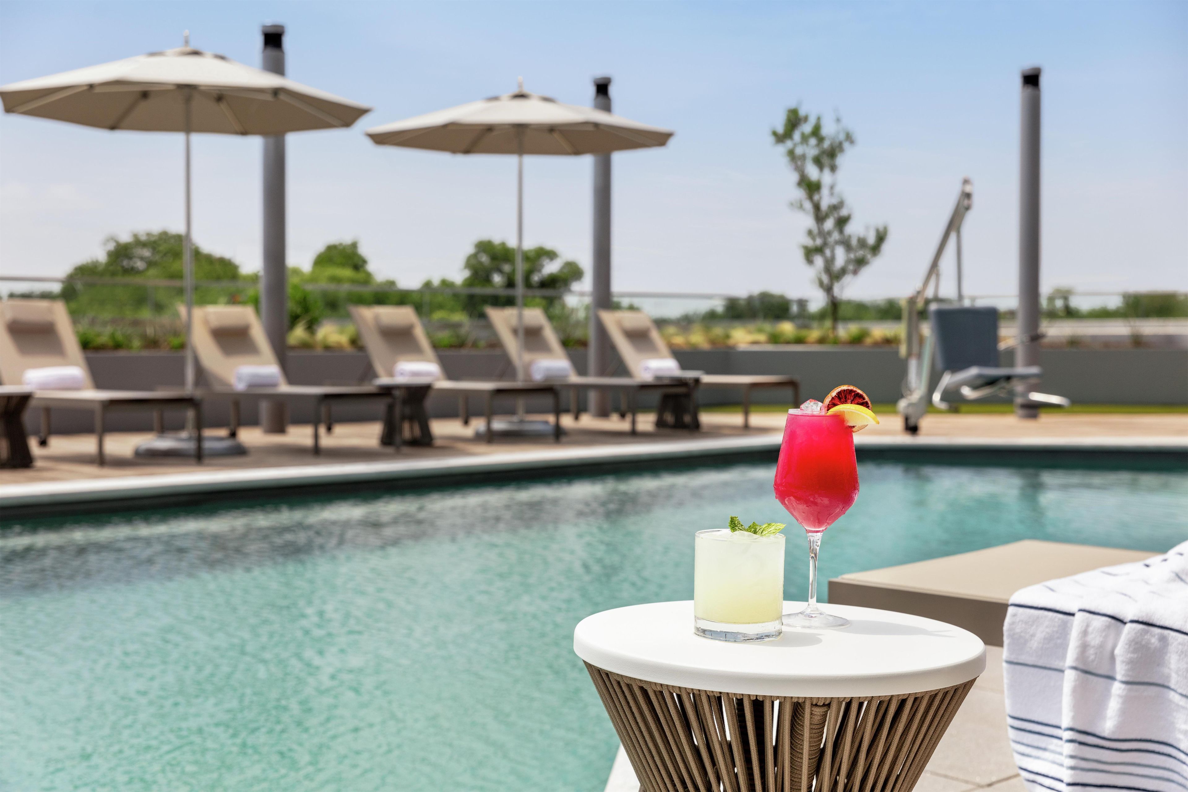 A poolside area with lounge chairs, umbrellas, and a table with drinks.