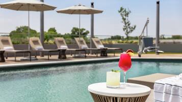 A poolside area with lounge chairs, umbrellas, and a table with drinks.