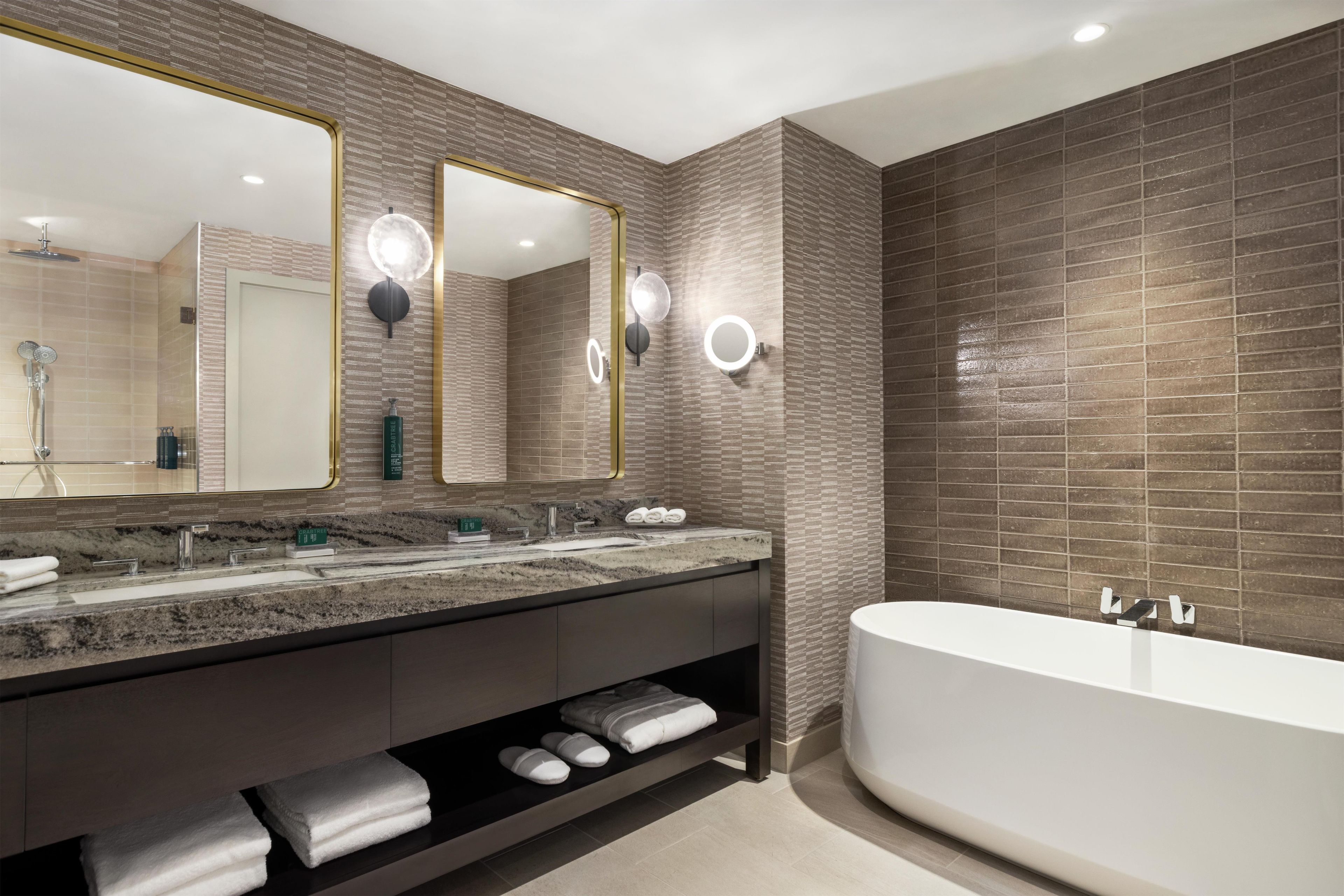 A modern bathroom with a large mirror, a bathtub, and a vanity with a marble countertop.