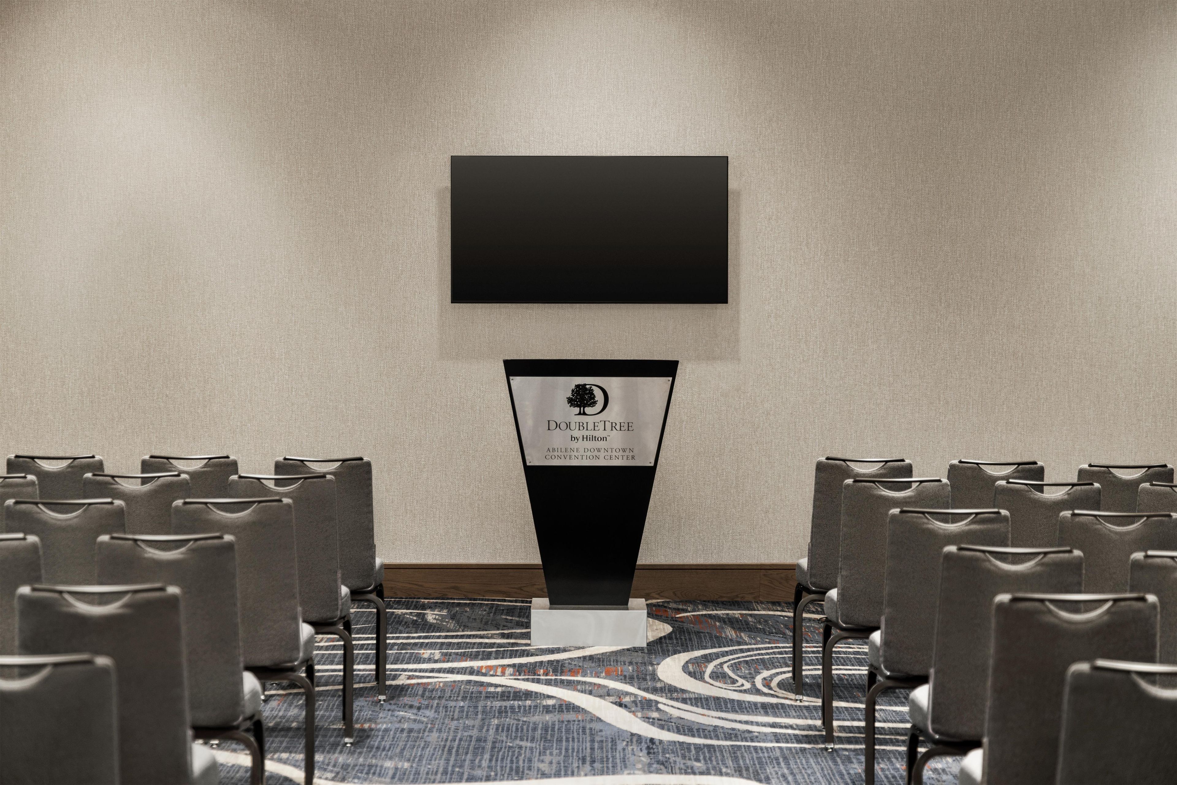 A conference room with rows of chairs, a podium, and a blank screen on the wall.