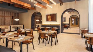 Un intérieur de restaurant moderne, avec des poutres en bois, des luminaires suspendus et un espace de restauration central agrémenté de tables et de chaises.