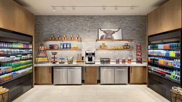 Un área de cocina moderna con dos refrigeradores llenos de bebidas, una cafetera y estantes con aperitivos y condimentos.