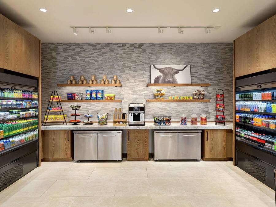Un área de cocina moderna con dos refrigeradores llenos de bebidas, una cafetera y estantes con aperitivos y condimentos.