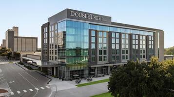 Un hôtel moderne à la façade en verre, appelé « DOUBLETREE by Hilton », qui dispose d’un vaste espace extérieur aménagé et d’une entrée imposante.