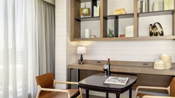 A hotel room with a wooden bookshelf, a table with a wine bottle, two chairs, and a lamp.