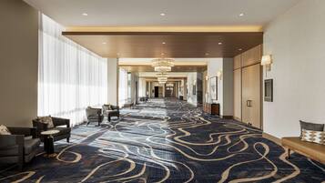 A hotel corridor with a patterned carpet, seating areas, and a chandelier.
