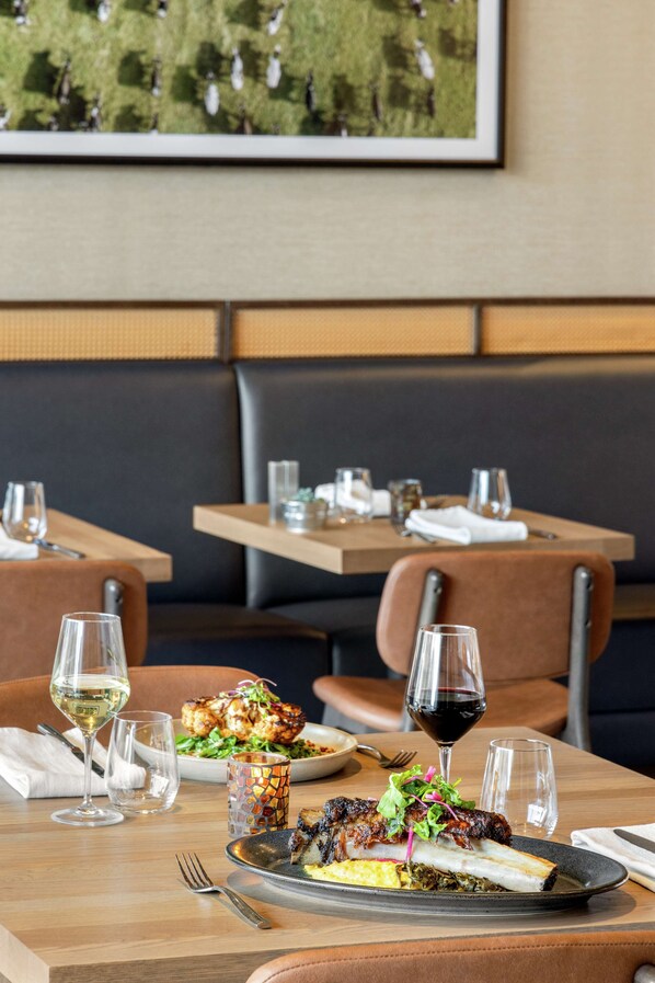 A restaurant setting with a dining table set for two, featuring a plate of food, wine glasses, and a decorative vase.
