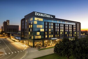 Un moderno hotel DoubleTree con fachada de vidrio, zona de estar al aire libre y vista despejada del paisaje urbano circundante.