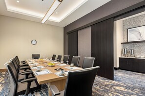 A conference room with a long table, chairs, a clock, and a coffee station.
