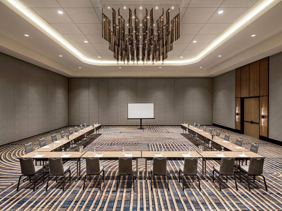 A conference room with a long table, chairs, a projector screen, and a patterned carpet.