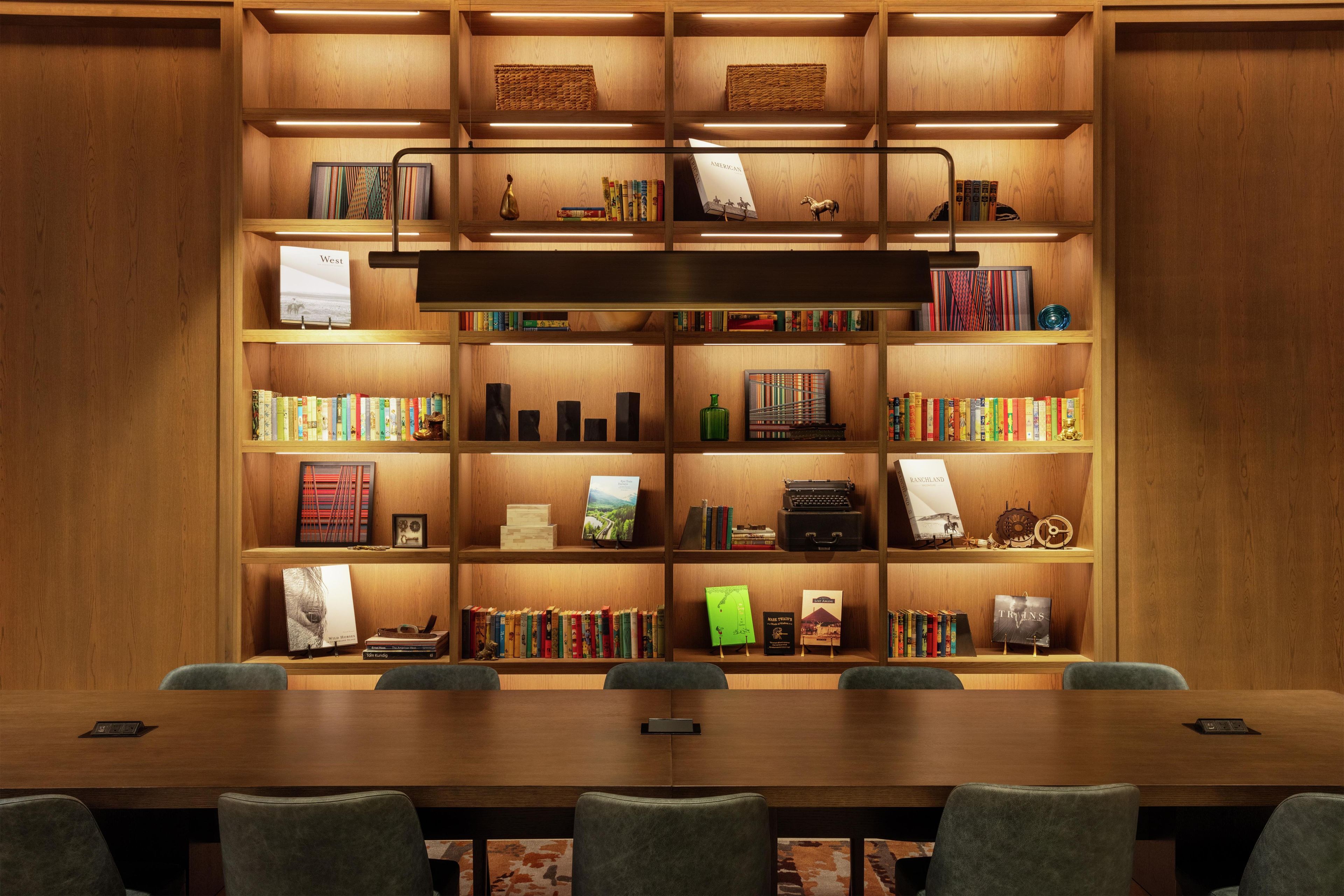 Ein gut beleuchtetes Holzregal mit Büchern und Dekorationsobjekten, ein Konferenztisch mit Stühlen und ein modernes Design.