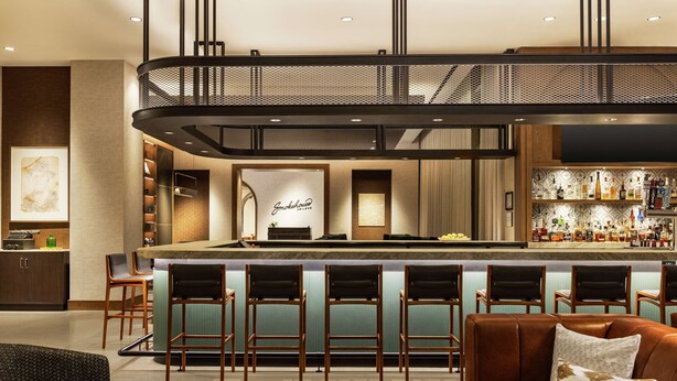 Un espace bar moderne doté d’un îlot central, de tabourets de bar et d’un coin salon avec un canapé et des fauteuils.