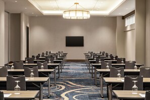 Une salle de conférence avec des rangées de tables et de chaises, une moquette à motifs et un luminaire au plafond.