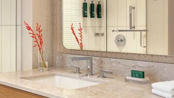 A bathroom with a marble sink, a mirror, and a glass vase with red flowers.