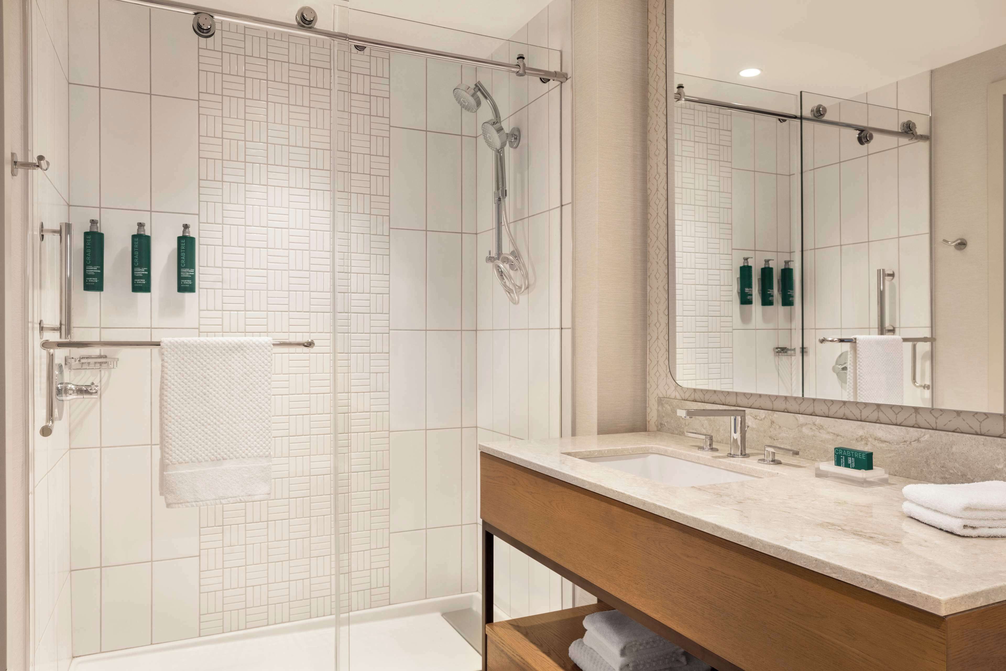 A modern bathroom with a glass-enclosed shower, a large mirror, and a vanity with a marble countertop.