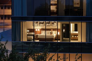 Habitación de hotel moderna con una cama grande, mesitas de noche y un baño visible a través del muro de cristal.