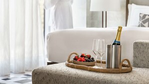 Une chambre d’hôtel avec un lit, une bouteille de champagne, des verres et un panier de fruits.