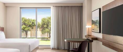 A hotel room with a bed, a desk, and a chair. There is a window with curtains, a lamp, and a picture on the wall.