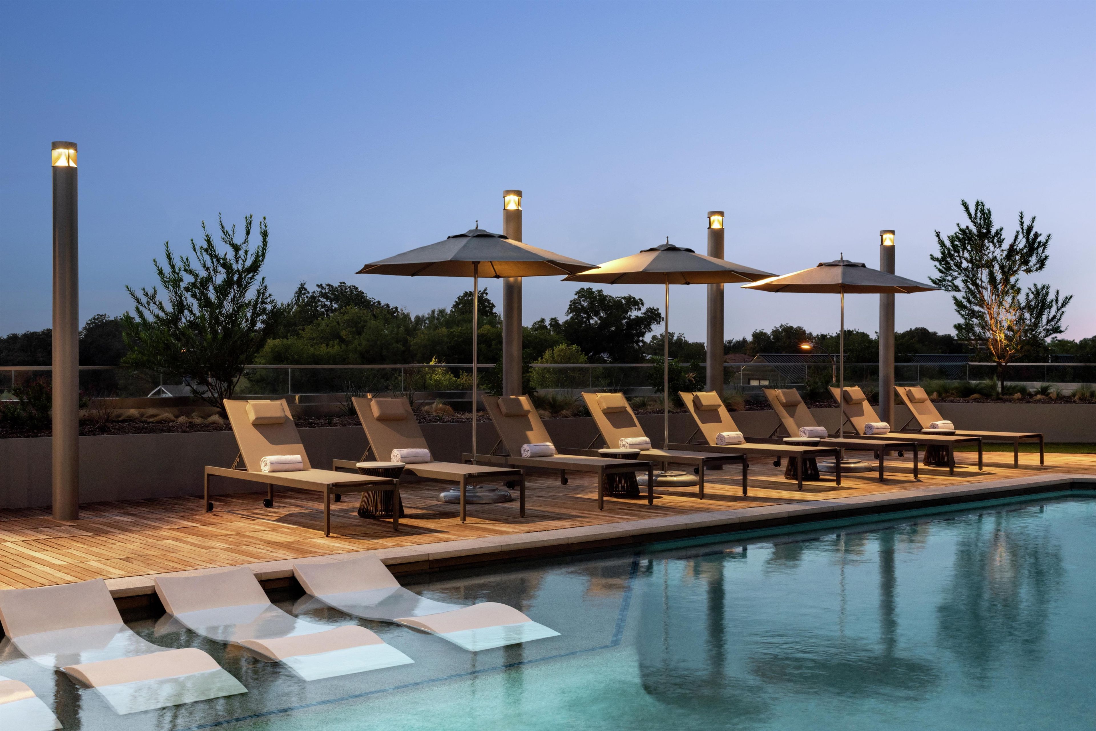 A poolside area with lounge chairs and umbrellas, a clear sky, and a calm pool.