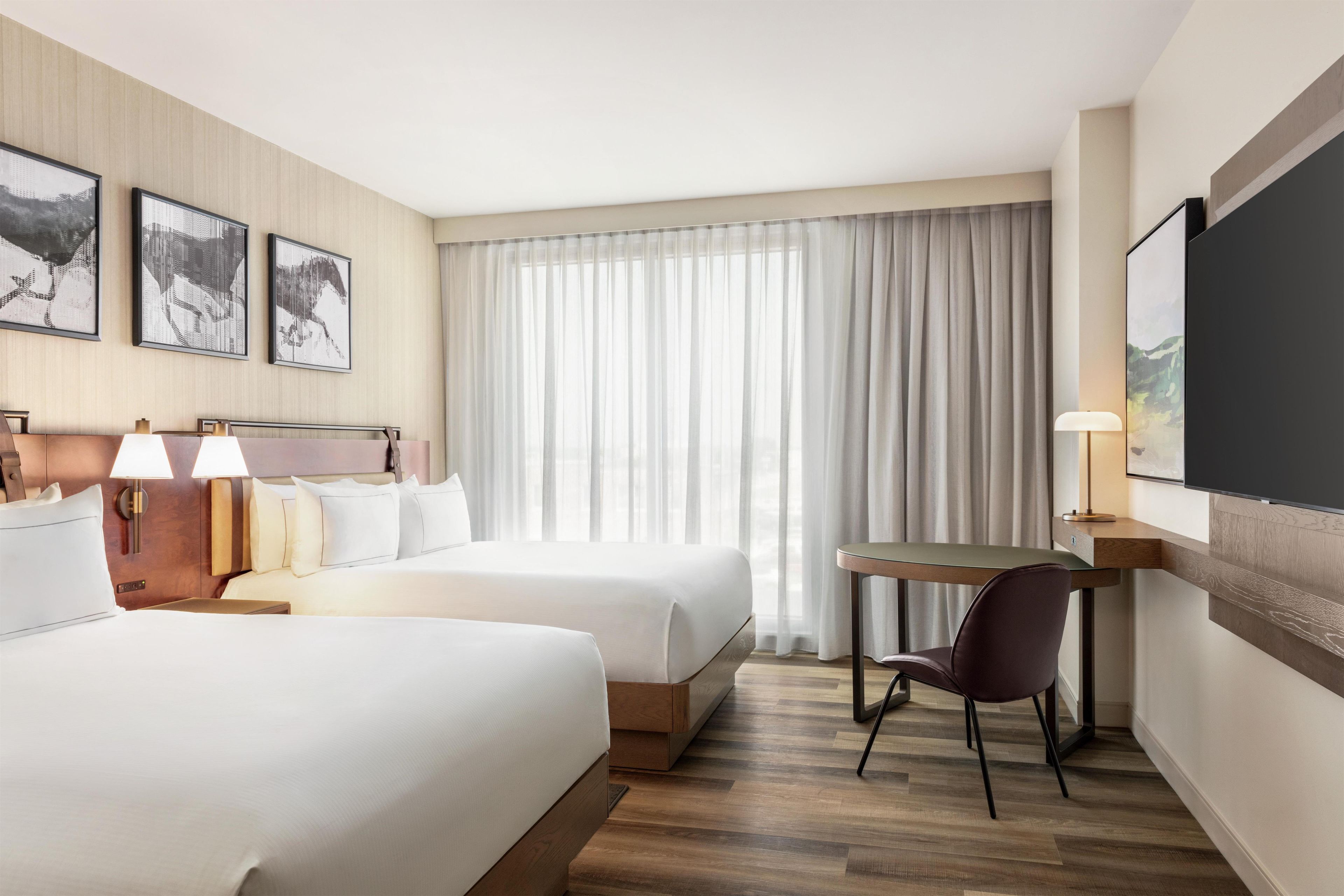 A hotel room with two beds, a desk, a chair, and a TV.