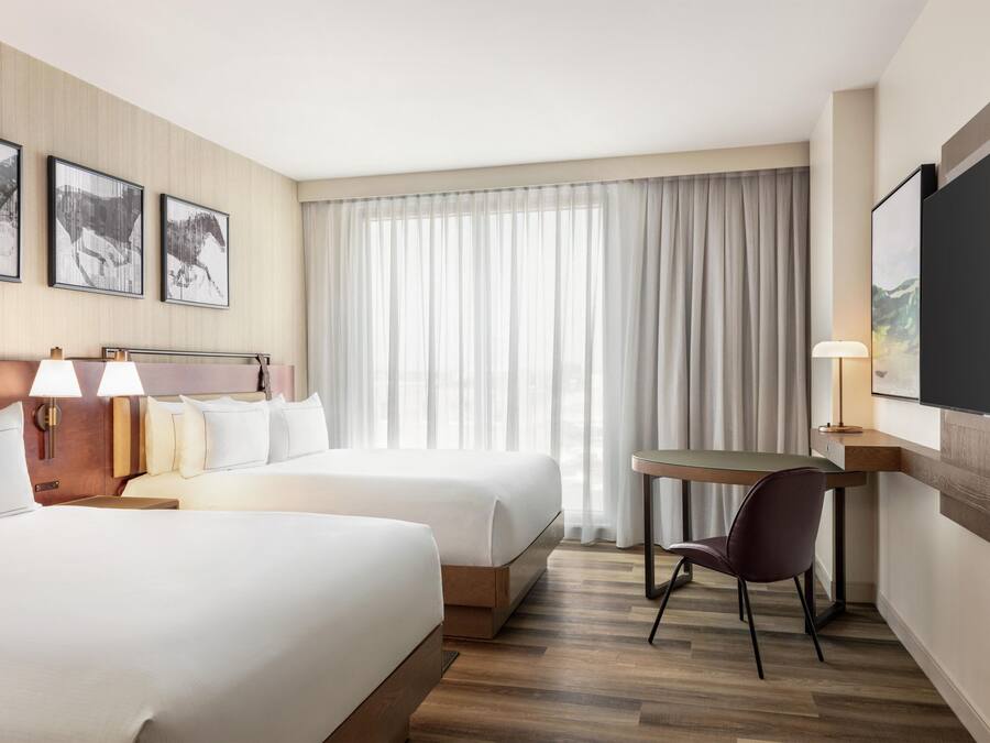Habitación de hotel con dos camas, un escritorio, una silla y un televisor.