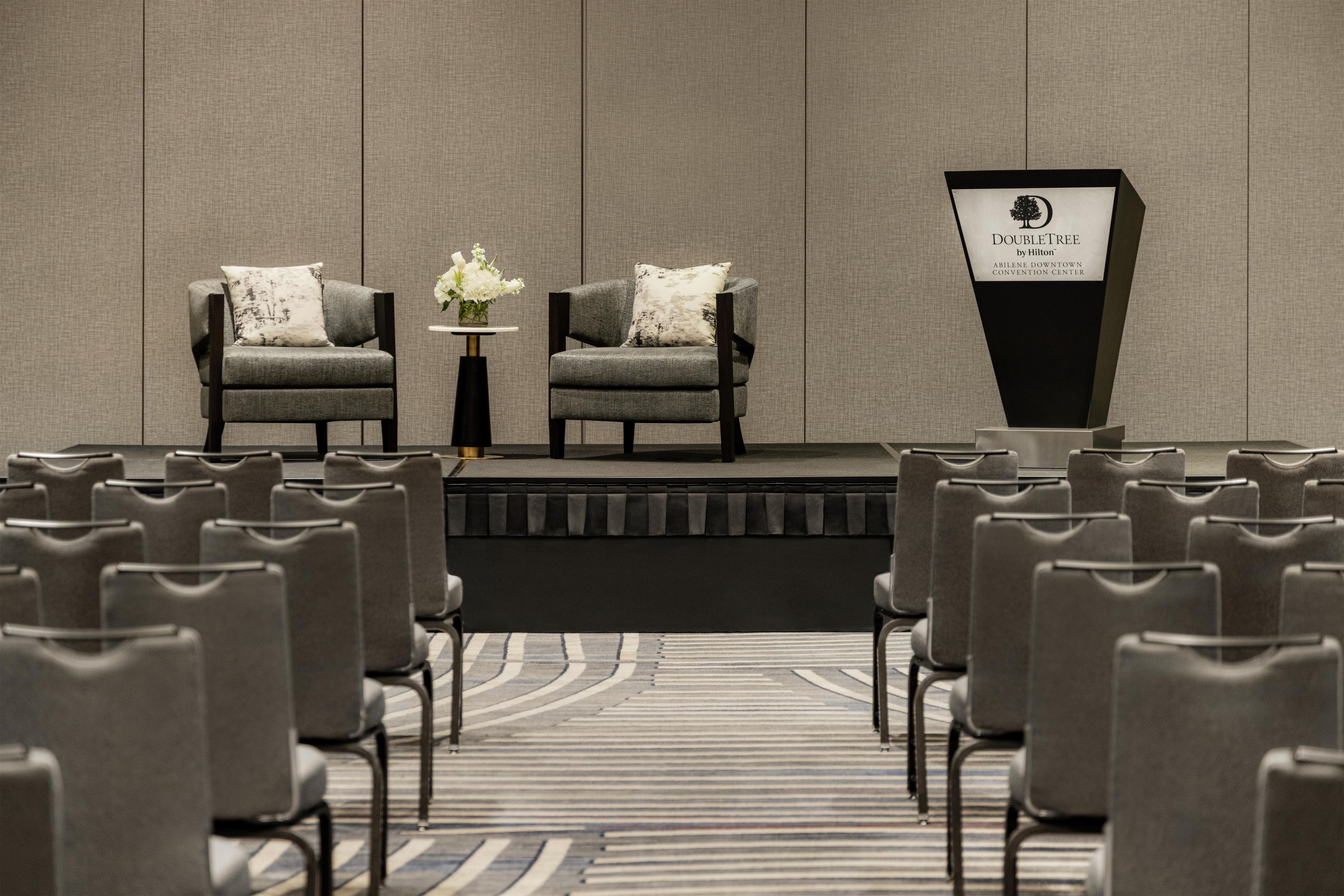 Une salle de conférence équipée de deux fauteuils, d’un pupitre et de rangées de chaises.