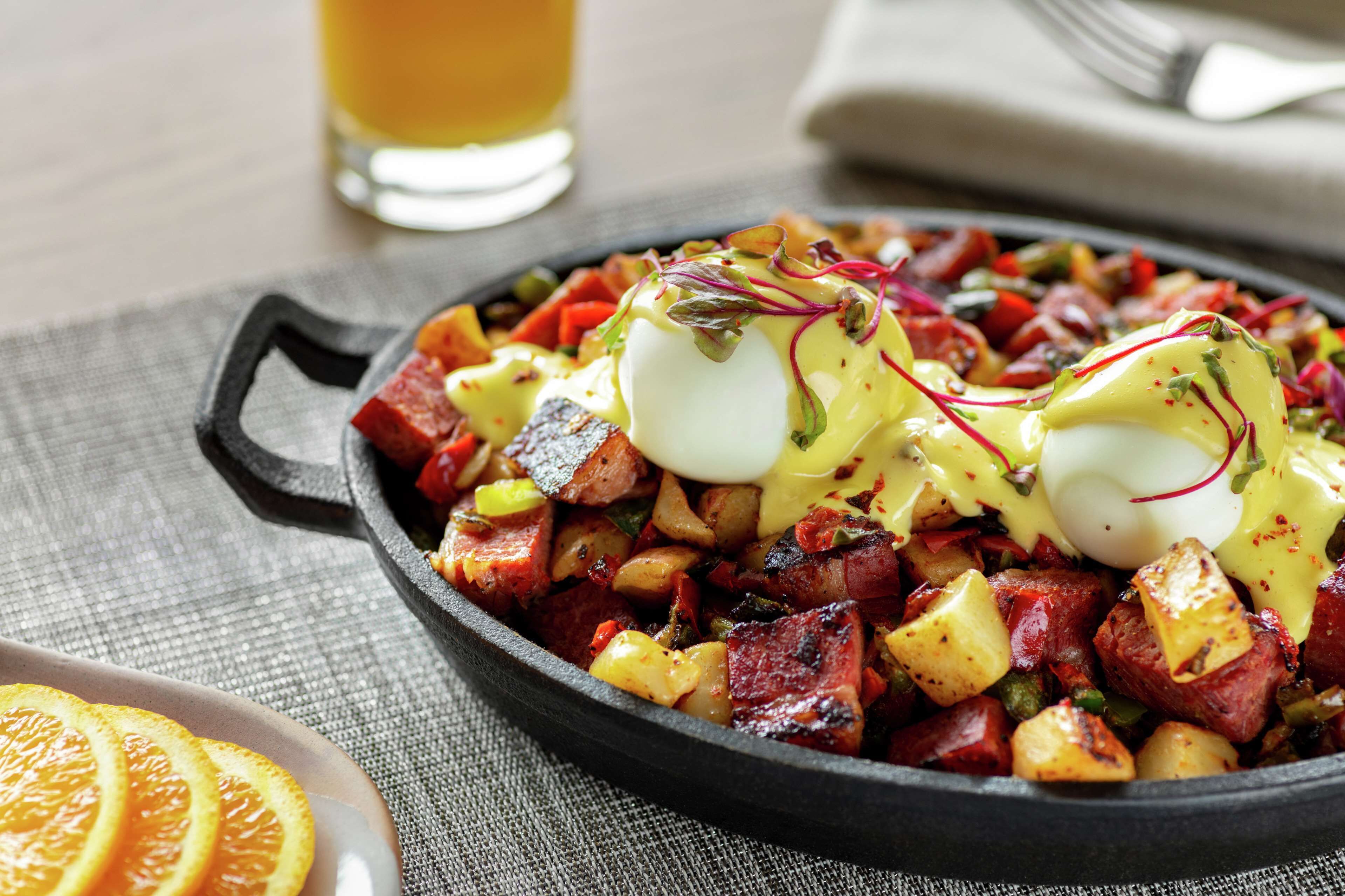 A skillet with a dish of diced potatoes, meat, and eggs, garnished with herbs and sauce.