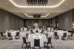Une salle de conférence dotée de plusieurs tables rondes, chacune étant agrémentée de chaises et de couverts.