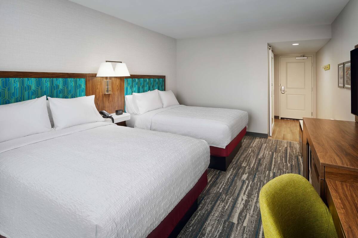 A hotel room with two beds, a desk, a chair, and a television.
