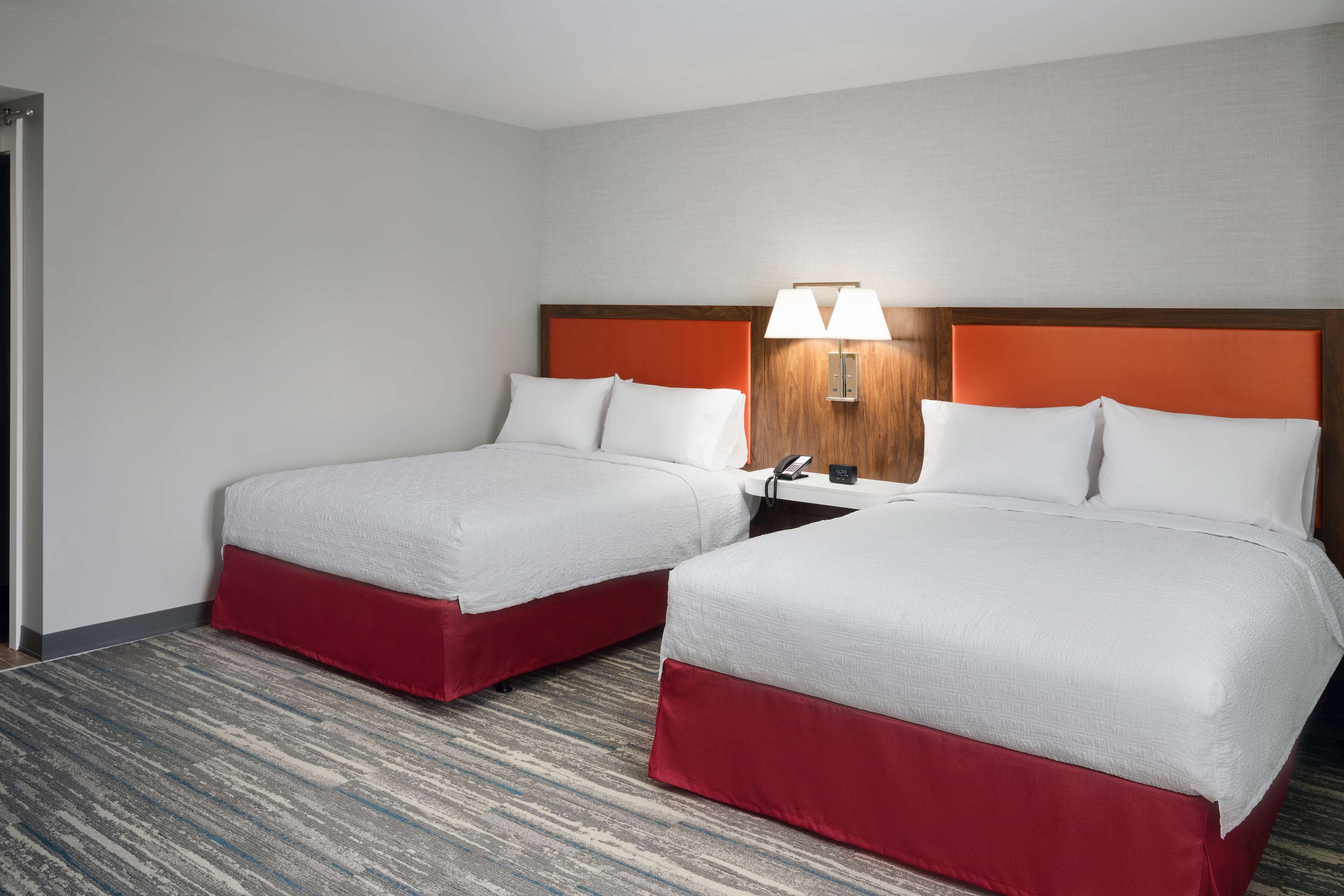 Ein Hotelzimmer mit zwei Betten, einem Holzkopfteil, einem Nachttisch mit Lampe und einem Telefon.