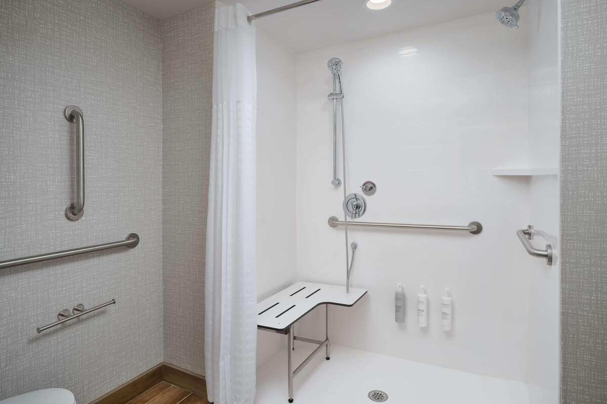 A modern bathroom with a walk-in shower, grab bars, and a small table with toiletries.